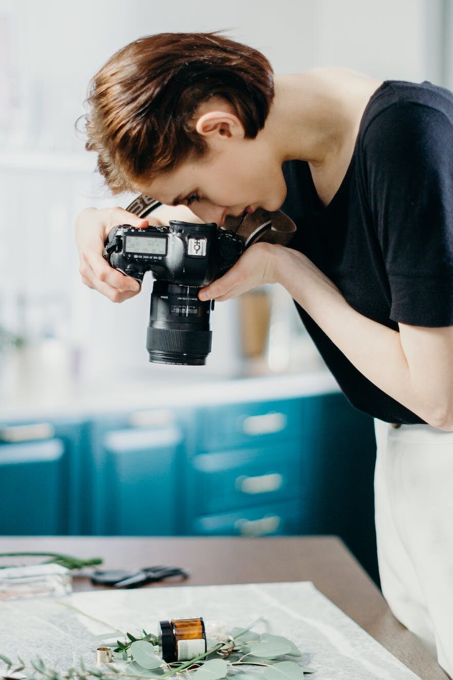 Woman Wearing Black Shirt Taking Picture of Flowers on Top of Table